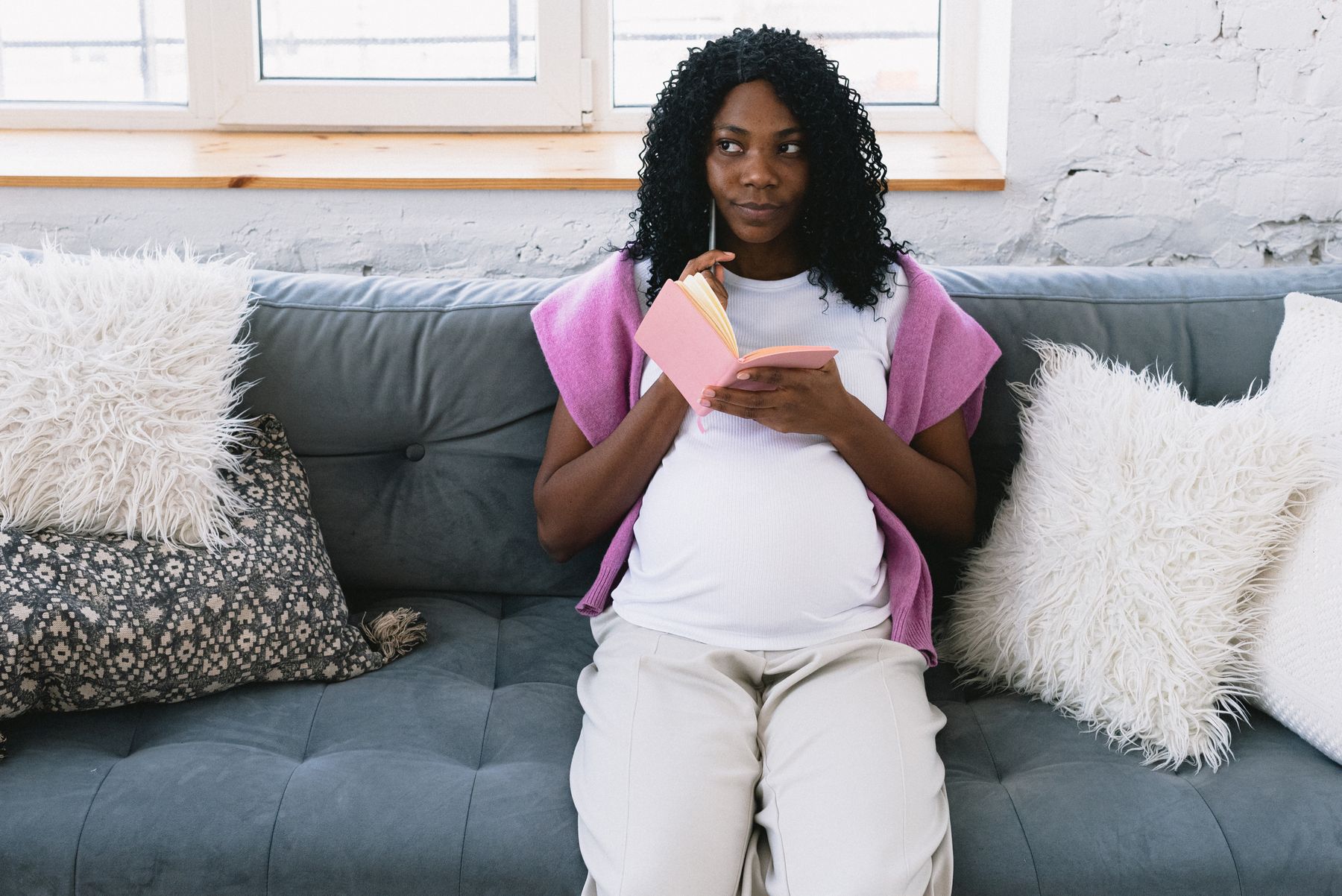 future maman assise, carnet ouvert sur les genoux, en train de réfléchir et noter des idées de prénoms